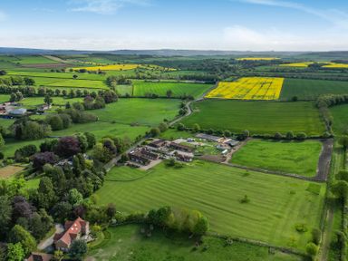 An aerial view of a farm surrounded by fields and trees at Sykes Lodge Malton