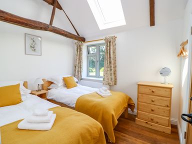 A bedroom with two single beds with yellow blankets and pillows wooden chest of drawers and a window at Sparrow Barn in Reepham