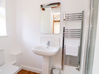 A bathroom with a sink under a mirror and a towel rack holding a folded towel at Sparrow Barn in Reepham