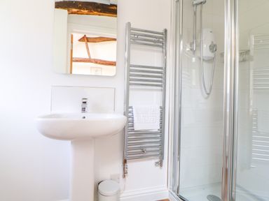 A bathroom with a pedestal sink a mirror a towel rail with a towel and a glass shower enclosure at Sparrow Barn in Reepham