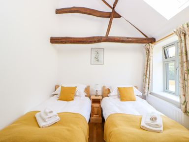 A bedroom with two single beds yellow pillows and blankets wooden beams on the ceiling at Sparrow Barn in Reepham