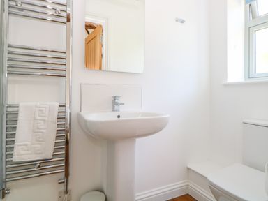 A bathroom with a pedestal sink a mirror a heated towel rail with a towel a window and a toilet at Sparrow Barn in Reepham