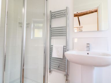 A bathroom with a shower enclosure a towel rail with a white towel and a sink with a mirror at Sparrow Barn in Reepham