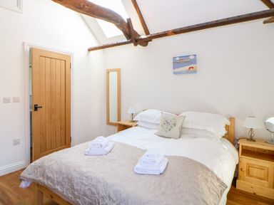 A bedroom with a bed with white linens and towels on a beige quilt beside wooden bedside tables and a wooden door at Sparrow Barn in Reepham