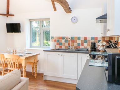 A kitchen and dining area with a wooden table set for four and white cabinets with a tiled backsplash at Sparrow Barn in Reepham