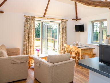 A living room with beige sofas and wooden dining table near open doors at Sparrow Barn in Reepham