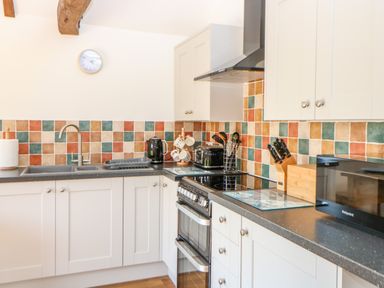 A kitchen with white cabinets a black countertop a stove a microwave a kettle and colorful tiled backsplash at Sparrow Barn in Reepham
