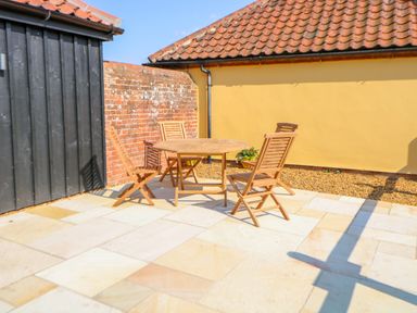 An outdoor patio with wooden chairs and a table near brick and yellow walls at Sparrow Barn in Reepham