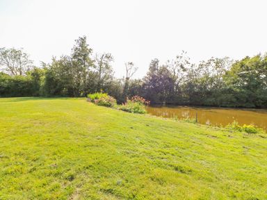 A grassy lawn with a flower bed and a pond surrounded by trees at Sparrow Barn in Reepham