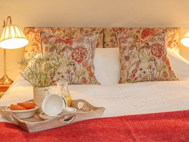 A bed with floral pillows a white quilt and a red throw with a tray holding a vase with flowers cups a jug and fruit at Rookwood in Drewsteignton