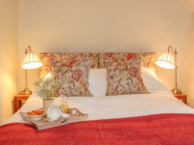 A bed with floral pillows and headboard a red blanket and bedside lamps at Rookwood in Drewsteignton