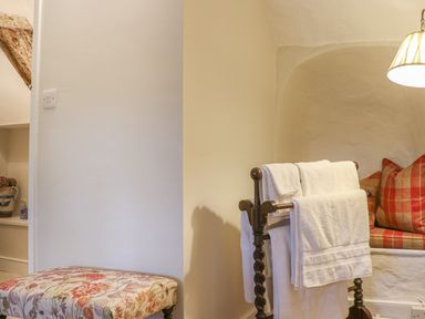 A corner with a floral patterned cushioned bench wooden towel rack with white towels and a built in seat with red plaid cushions at Rookwood in Drewsteignton