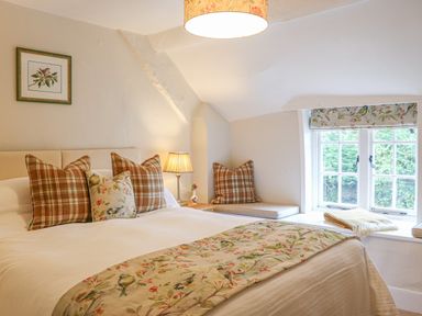 A bedroom with a bed pillows lamp window seat and floral curtains at Rookwood in Drewsteignton