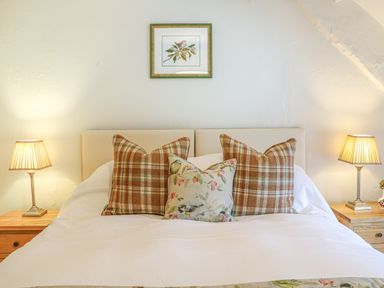 A bedroom with a bed with plaid and floral pillows and two bedside tables with lamps at Rookwood in Drewsteignton