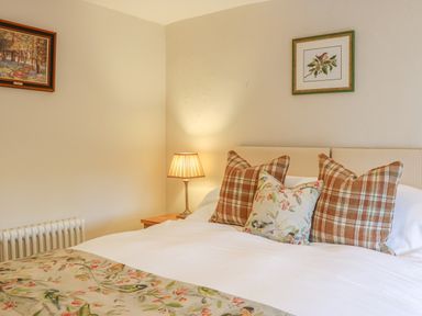 A bedroom with a bed with patterned pillows a lamp on a bedside table and framed pictures on the wall at Rookwood in Drewsteignton