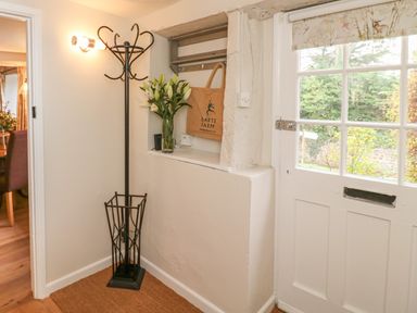 An entrance hall with a coat stand a vase of flowers a wall hook shelf a tote bag and a white door with glass panes at Rookwood in Drewsteignton