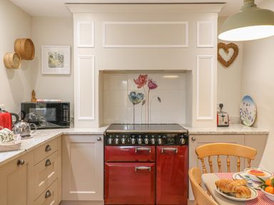 A kitchen with a red stove oven microwave kettle toaster wooden chair and table at Rookwood in Drewsteignton