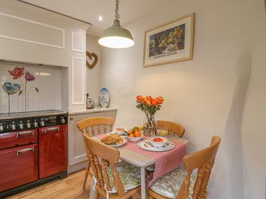 A kitchen corner with a small dining table set with food and flowers and a red stove at Rookwood in Drewsteignton