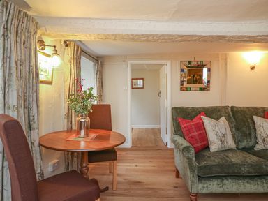 A room with a round wooden table and two brown chairs next to a green sofa with cushions and an open doorway at Rookwood in Drewsteignton