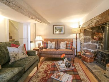 A living room with two sofas a plaid ottoman a stone fireplace and wooden beams at Rookwood in Drewsteignton