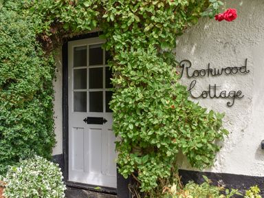 A white wooden door surrounded by green vines with a sign reading Rookwood Cottage on the wall at Rookwood in Drewsteignton