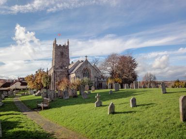 A church with a tower and surrounding gravestones in a grassy churchyard at Rookwood in Drewsteignton