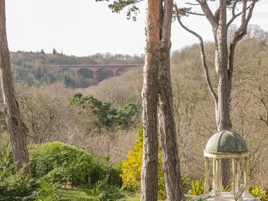 A garden with trees shrubs a small domed gazebo and a bridge in the background at Daffodil Lodge in Saltburn-by-the-Sea