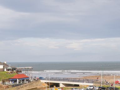 A coastal scene with a pier extending into the sea a building with a red roof a bridge over a small waterway and parked cars at Daffodil Lodge in Saltburn-by-the-Sea