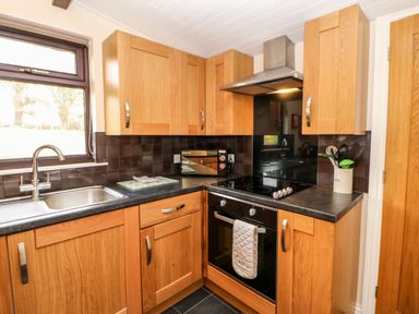 A kitchen with wooden cabinets a black countertop a stainless steel sink an oven and a microwave at Daffodil Lodge Saltburn-by-the-Sea
