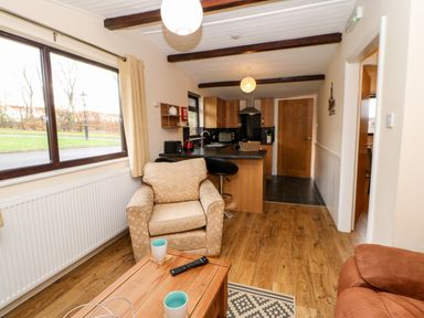 A living room with beige armchair coffee table cups and open kitchen with wooden cabinets at Daffodil Lodge in Saltburn-by-the-Sea