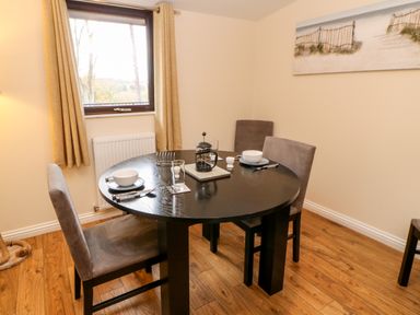 A dining room with a round table set for two near a window with beige curtains at Daffodil Lodge in Saltburn-by-the-Sea