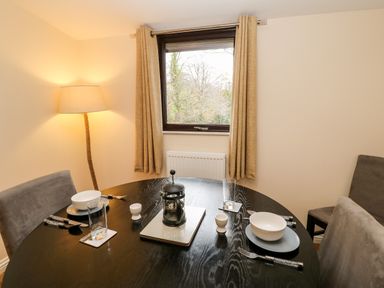 A dining area with a round table set for two with bowls glasses and cutlery next to a window with curtains and a floor lamp at Daffodil Lodge in Saltburn-by-the-Sea