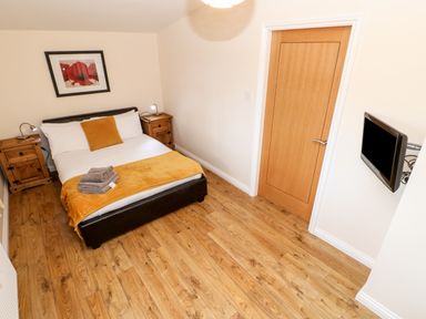 A bedroom with a double bed with yellow bedding beside wooden bedside tables with lamps and a wall-mounted TV at Daffodil Lodge in Saltburn-by-the-Sea