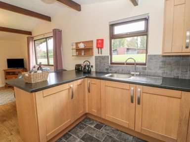 A kitchen with wooden cabinets a black countertop a sink and a window overlooking greenery at Orchid Lodge in Saltburn-by-the-Sea