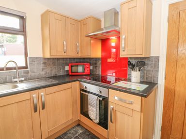 A kitchen with wooden cabinets a sink a red microwave a stove with an oven and cooking utensils at Orchid Lodge in Saltburn-by-the-Sea