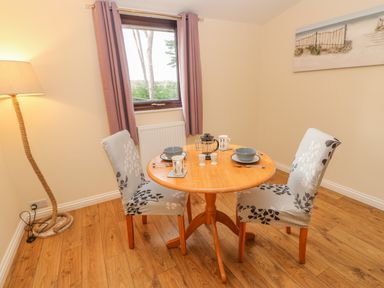 A dining area with a round wooden table and two patterned chairs near a window with curtains at Orchid Lodge in Saltburn-by-the-Sea