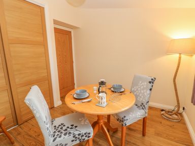 A small dining area with a round wooden table set for two and two chairs with patterned covers at Orchid Lodge in Saltburn-by-the-Sea