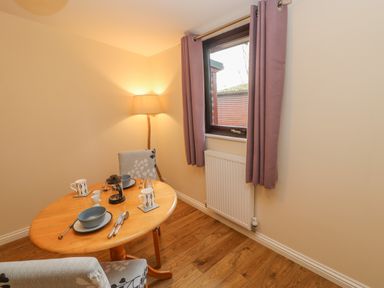 A small dining area with a wooden table set for two near a window with purple curtains and a standing lamp at Orchid Lodge in Saltburn-by-the-Sea