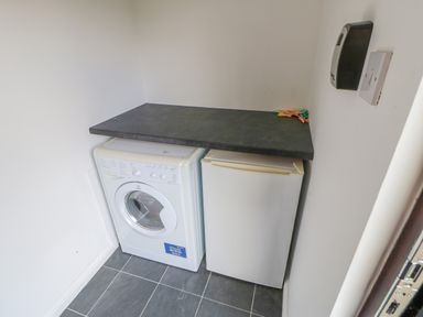 A small utility room with a washing machine and a fridge under a black countertop with clothespins on it at Orchid Lodge in Saltburn-by-the-Sea
