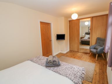 A bedroom with a bed with folded towels on it a gray armchair a wall-mounted TV and wooden wardrobes with a mirrored door at Orchid Lodge in Saltburn-by-the-Sea