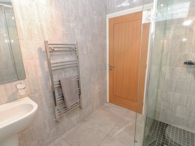 A bathroom with a wooden door a glass shower enclosure a chrome towel rack with a gray towel and a white sink at Orchid Lodge in Saltburn-by-the-Sea
