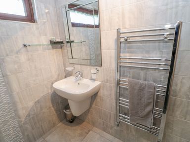 A bathroom with a wall-mounted sink mirror towel rack and window at Orchid Lodge in Saltburn-by-the-Sea