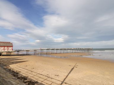A sandy beach with a long pier extending into the sea and a building on stilts at the edge of the beach at Foxglove Lodge in Saltburn-By-The-Sea
