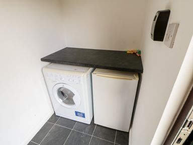A small utility room with a washing machine and a fridge under a black countertop at Foxglove Lodge in Saltburn-By-The-Sea