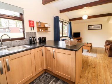 A kitchen area with a sink toaster and kettle next to a living room with a coffee table sofa and television at Foxglove Lodge in Saltburn-By-The-Sea