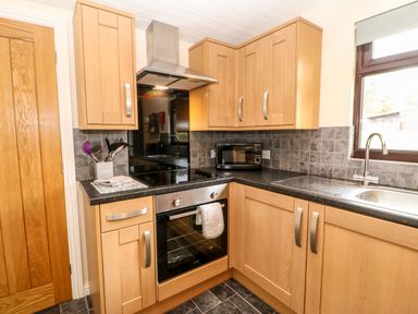A kitchen with wooden cabinets black countertop microwave oven stove and a window at Foxglove Lodge in Saltburn-By-The-Sea