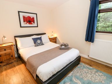 A bedroom with a double bed between two wooden bedside tables with lamps and a window with blue curtains at Foxglove Lodge in Saltburn-By-The-Sea