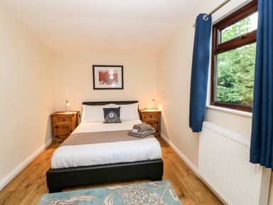 A bedroom with a double bed between two wooden nightstands with lamps and a window with blue curtains at Foxglove Lodge in Saltburn-By-The-Sea