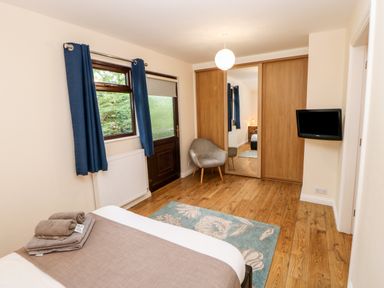 A bedroom with a bed and folded towels a chair blue curtains wooden floor and a wall-mounted TV at Foxglove Lodge in Saltburn-By-The-Sea