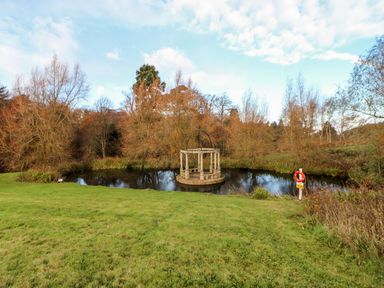 A small pond with a stone gazebo structure in the center and grassy area with trees around at Foxglove Lodge in Saltburn-By-The-Sea